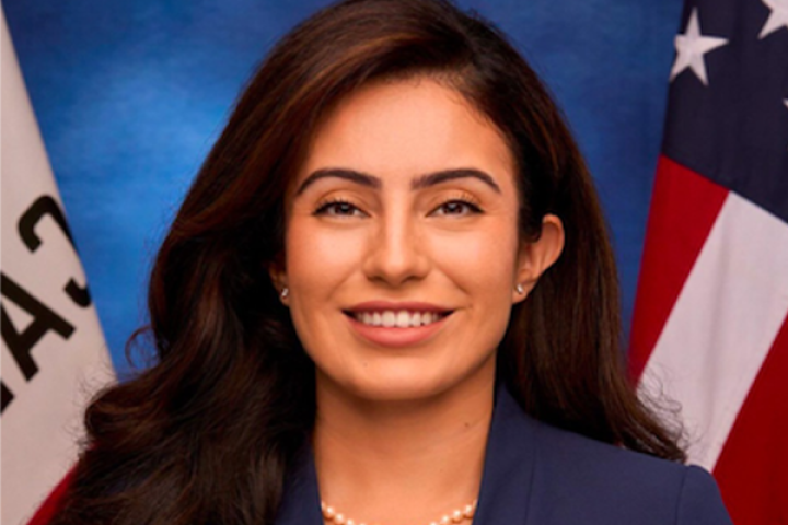 Senator Sasha Renée Pérez wearing a blue blazer standing in front of a United States and California Flag